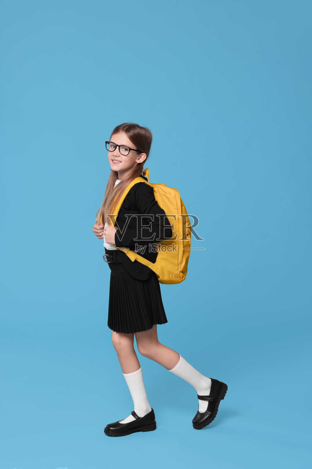 快乐的女学生背着浅蓝色背景的背包照片摄影图片