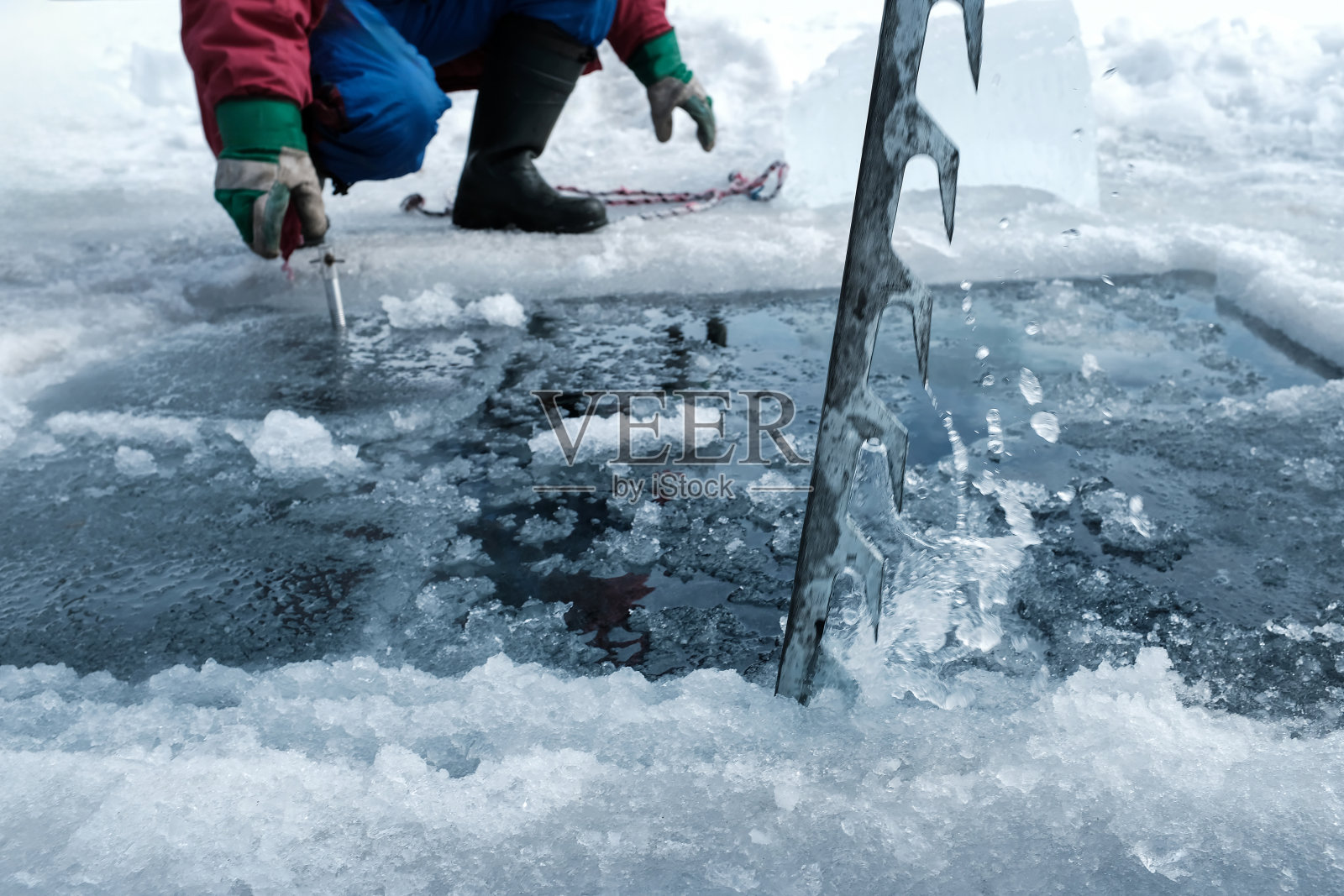 一名男子为了潜水而锯开一个冰洞，取出冰块照片摄影图片