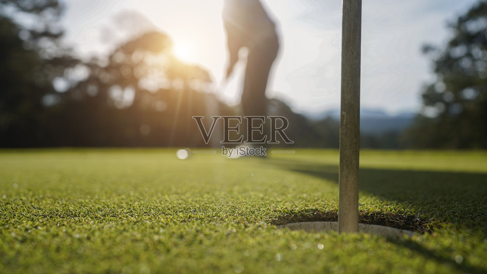 高尔夫球手在绿色的高尔夫球场上击球，镜头闪耀在夕阳西下的黄昏时分。照片摄影图片