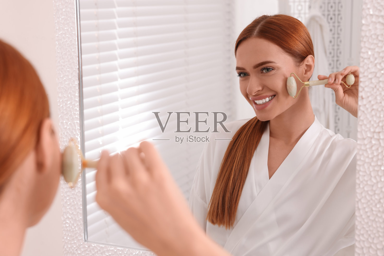 年轻女子在浴室镜子旁用玉辊按摩脸部照片摄影图片