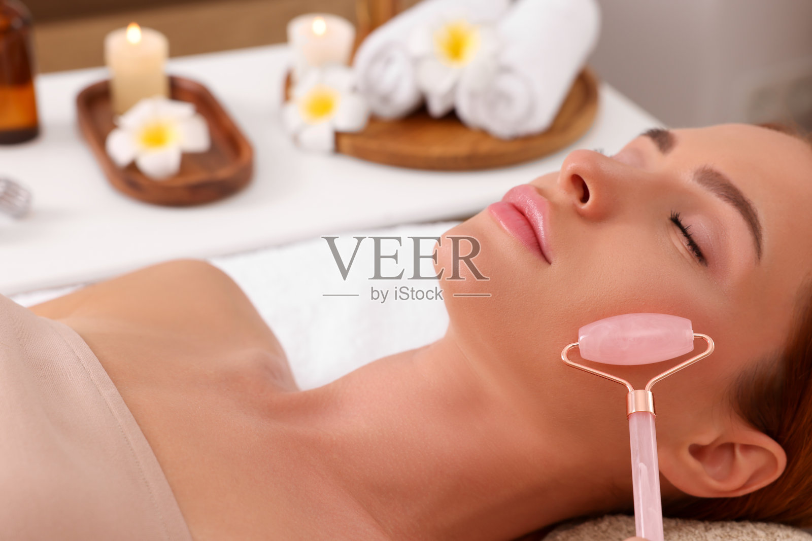 年轻女子在美容院用玫瑰石英滚筒接受面部按摩，特写照片摄影图片