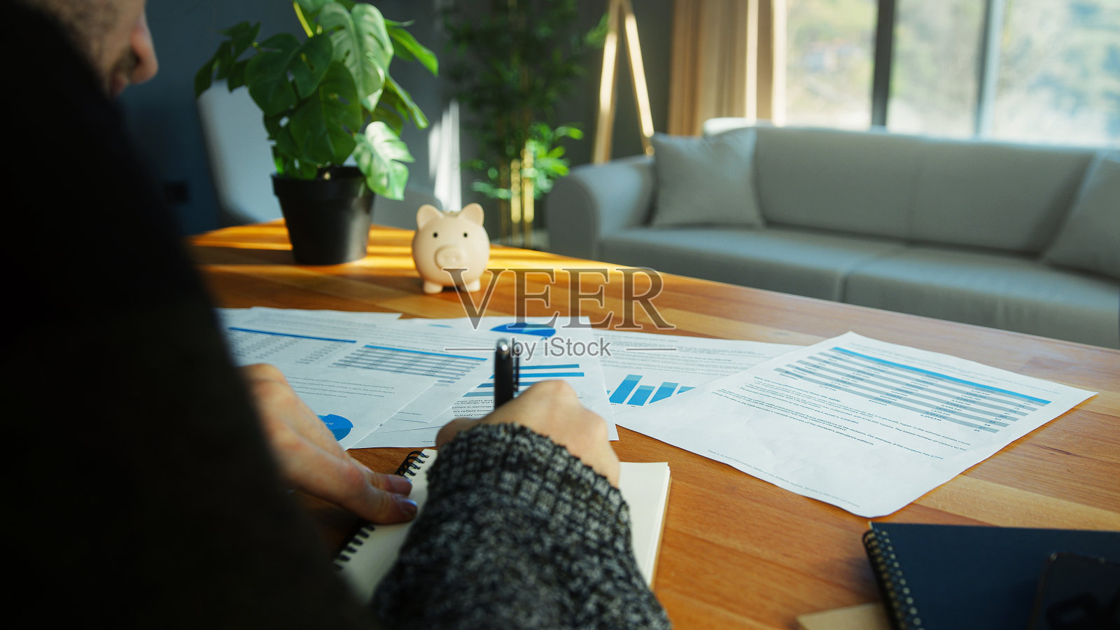 年轻的商人戴着无边帽在现代家庭办公室的桌子上工作，用图形模板和报告，在笔记本上写字。肩膀上的特写镜头照片摄影图片