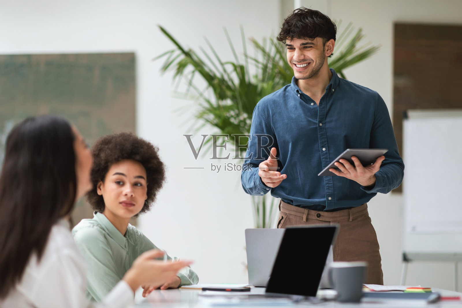 带着数码平板电脑的微笑商人在室内与多民族同事交谈照片摄影图片