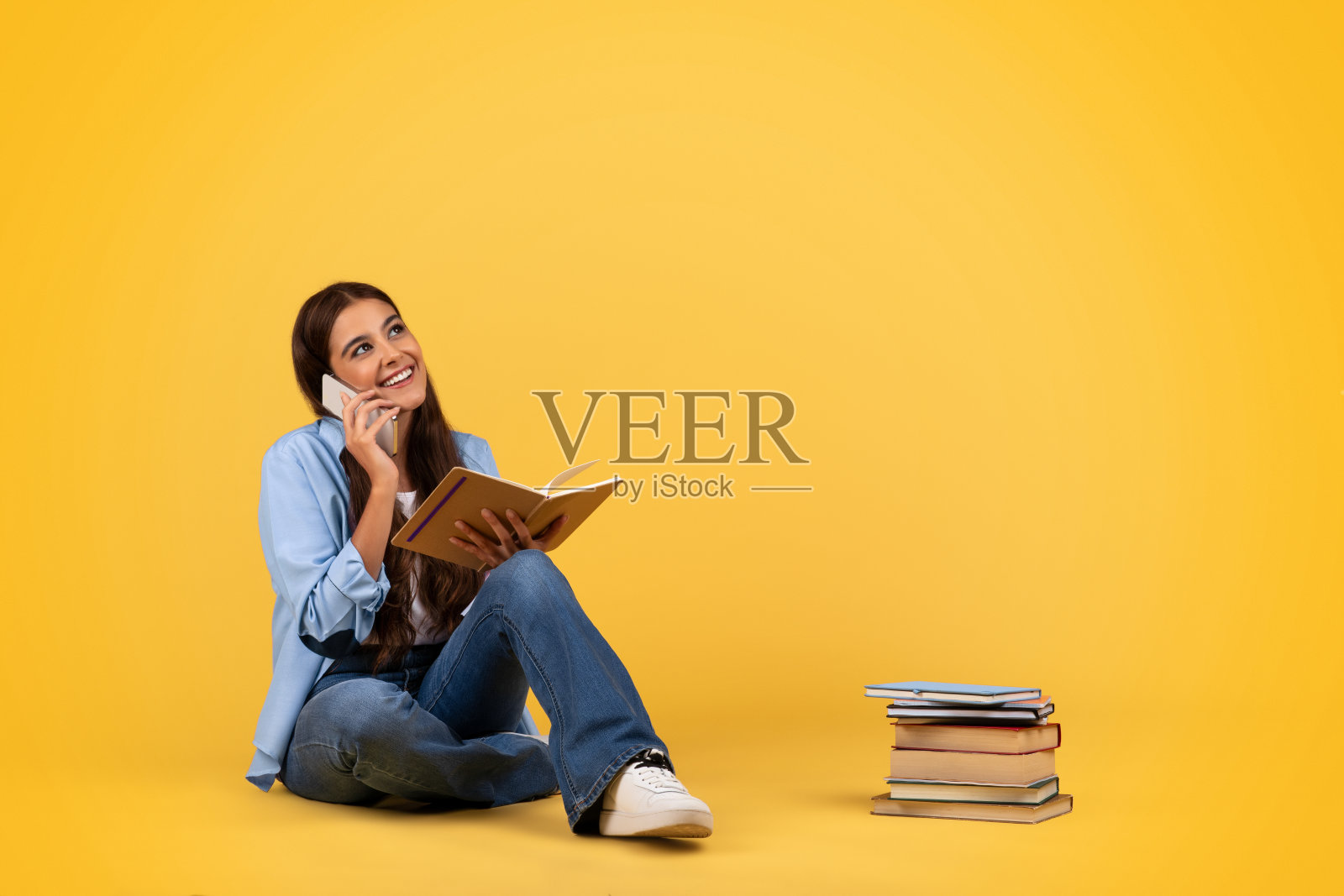 积极的青少年女学生用智能手机打电话，用书本学习，坐在地板上照片摄影图片