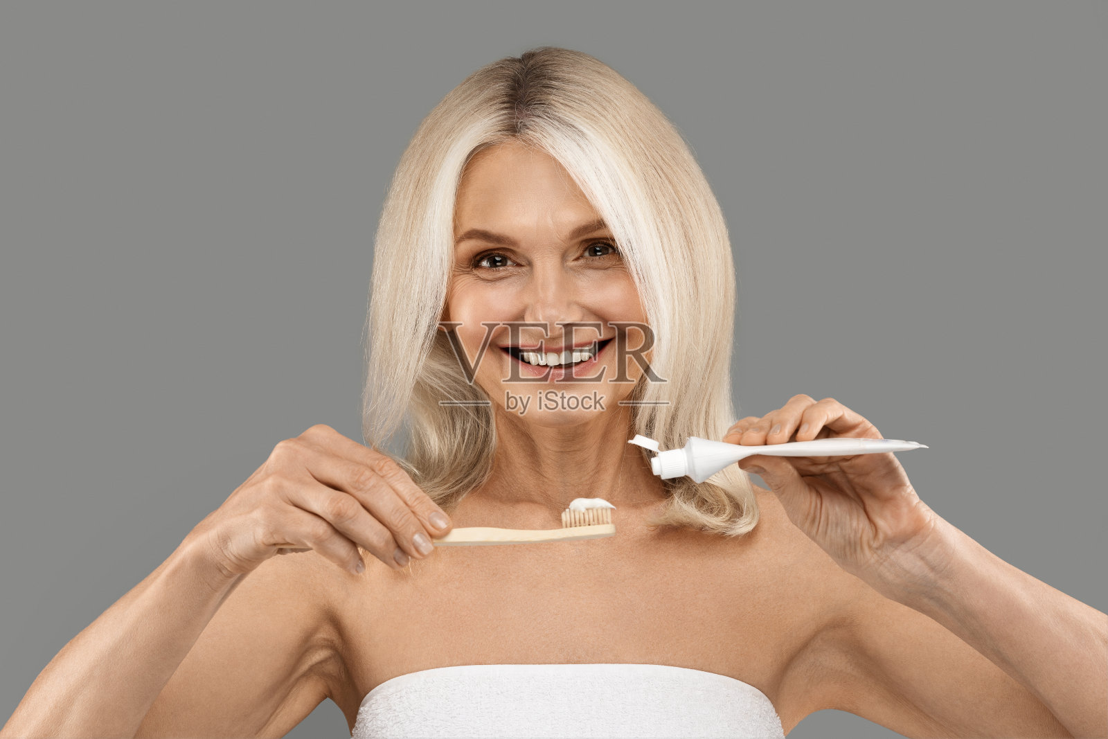 日常牙齿护理。美丽成熟的女人把牙膏倒在牙刷上照片摄影图片