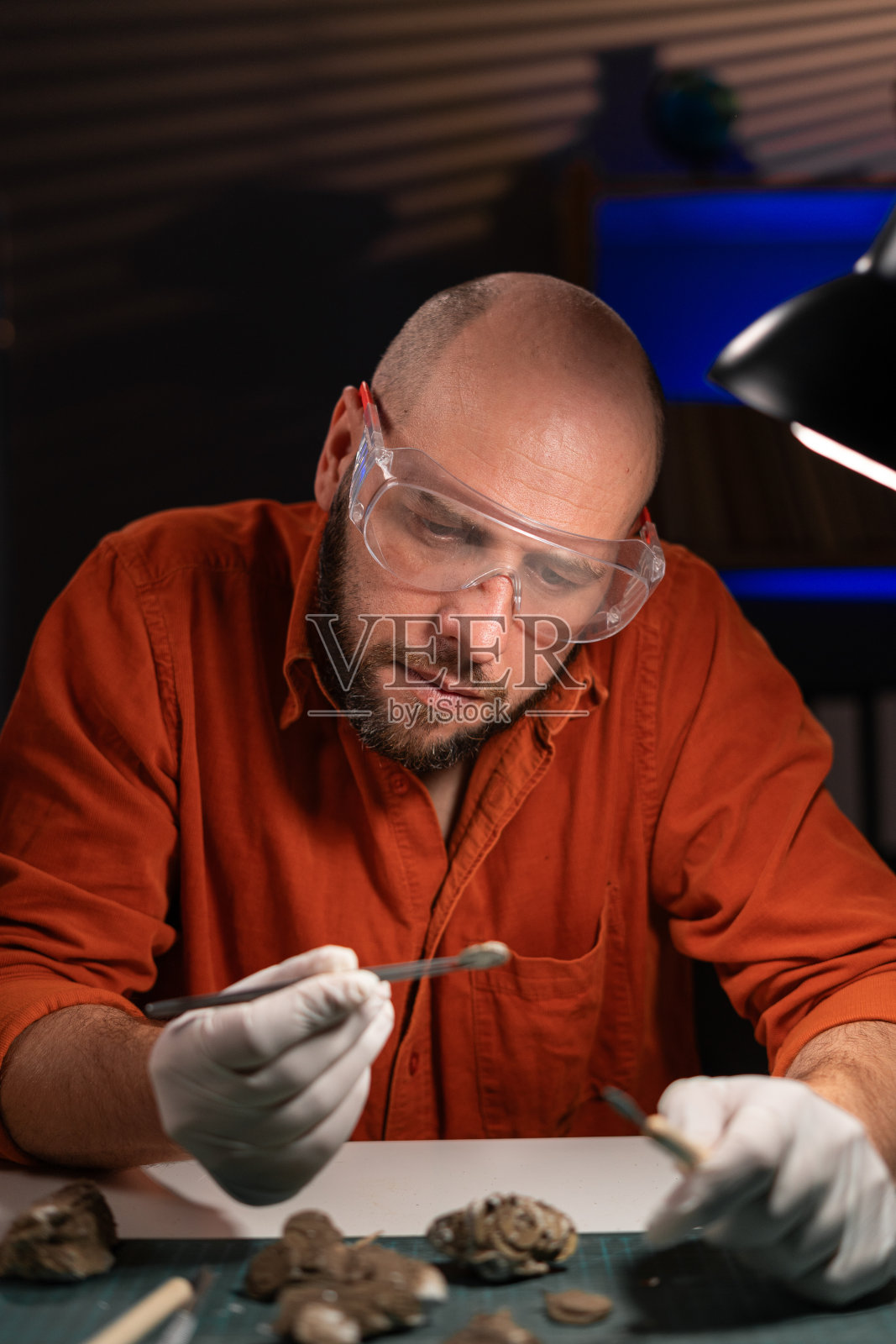 留胡子的科学家考古学家在办公室工作到深夜时，拿着考古发掘中发现的古钱币化石。照片摄影图片