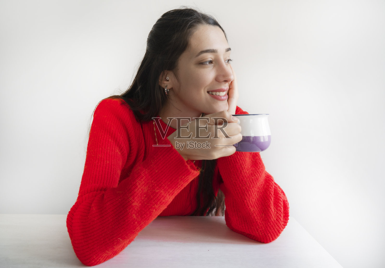 一个年轻的女孩坐在一张白色的桌子前，手里拿着一个咖啡杯照片摄影图片