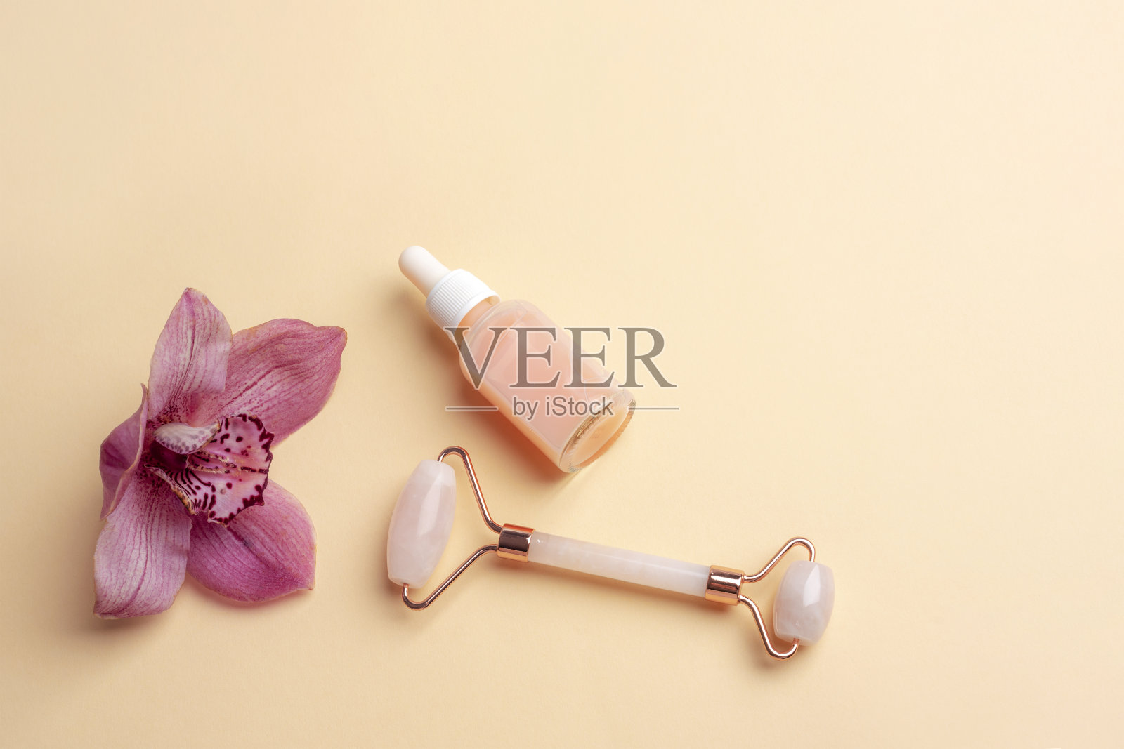 粉红色的精华液瓶，玫瑰石英水晶面部滚筒和兰花在米色背景。俯视图，平面布局，复制空间照片摄影图片