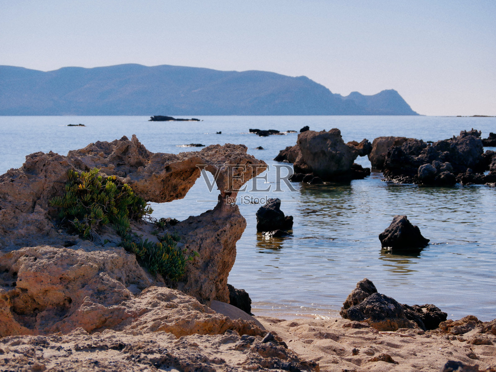 希腊克里特岛海滩上有一个洞的岩石。照片摄影图片