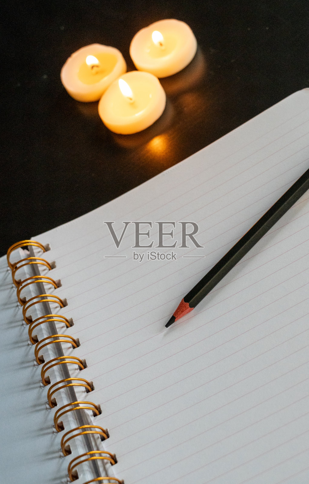 打开螺旋笔记本在白色的纸上，用铅笔放在黑色的桌子上，用三支点燃的小蜡烛照片摄影图片