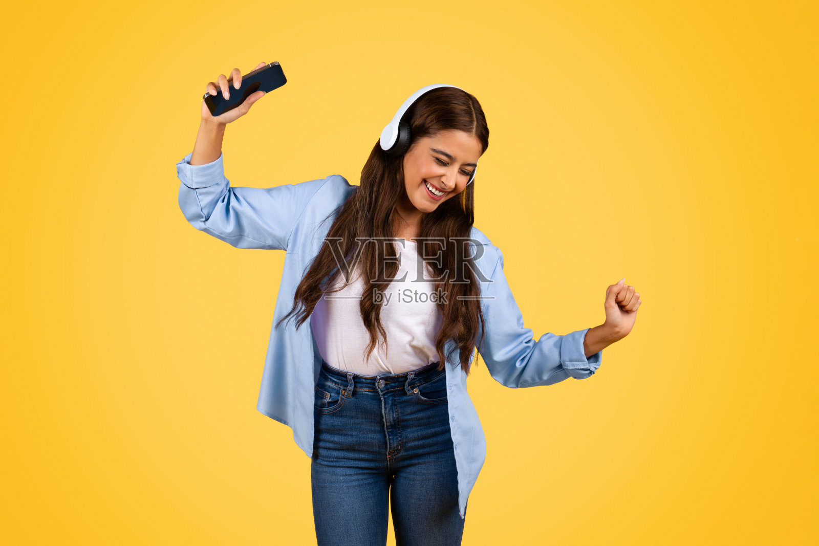 开朗的年轻女学生有智能手机，耳机，跳舞，享受音乐，生活方式照片摄影图片