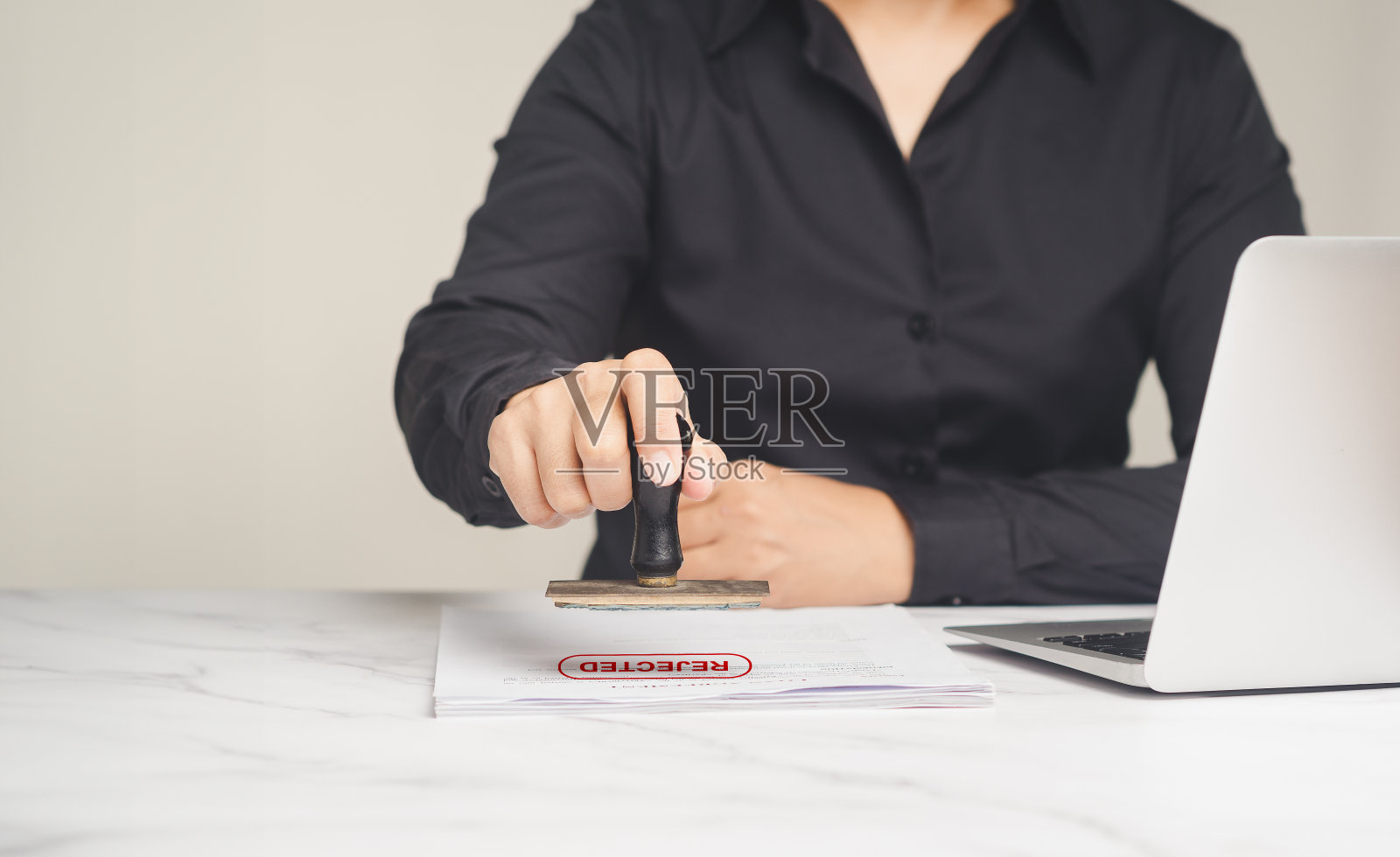 女商人坐在桌旁为被拒绝的文件盖章。照片摄影图片