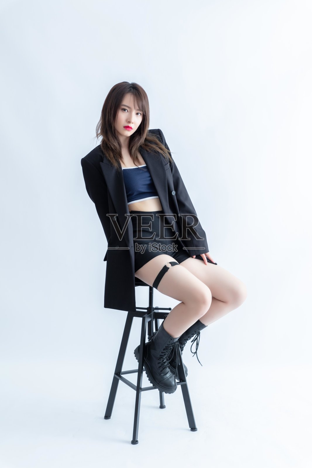 一个穿着黑色西装外套和蓝色运动胸罩的年轻女子坐在凳子上。照片摄影图片