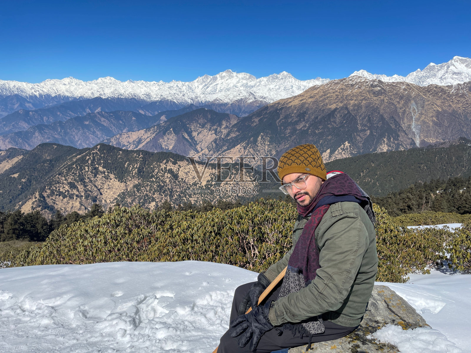 一个男人坐在积雪覆盖的山顶上，背景是积雪覆盖的山脉照片摄影图片