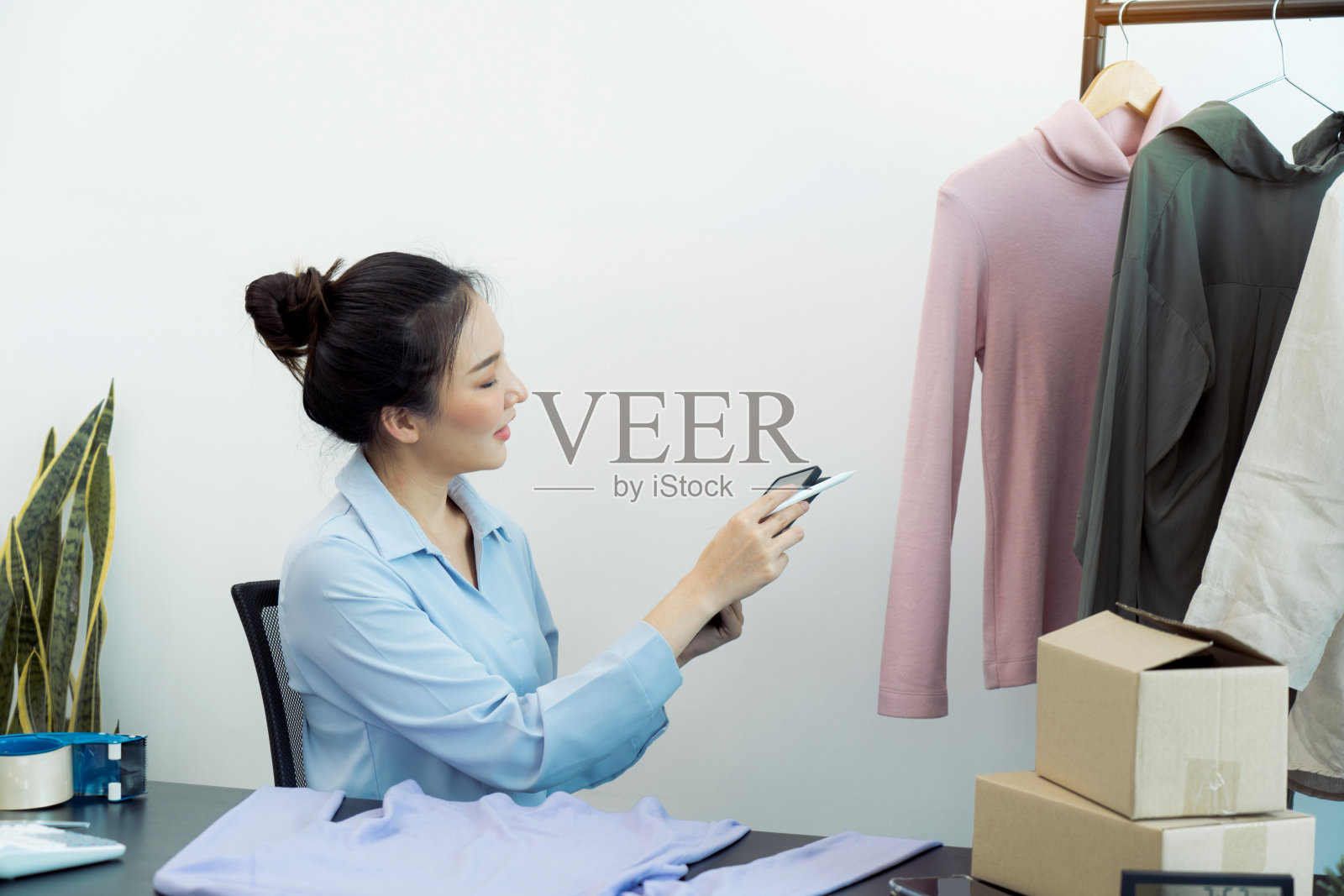 一位亚洲企业家正在通过她的平板电脑检查她仓库里剩余的衣服。照片摄影图片