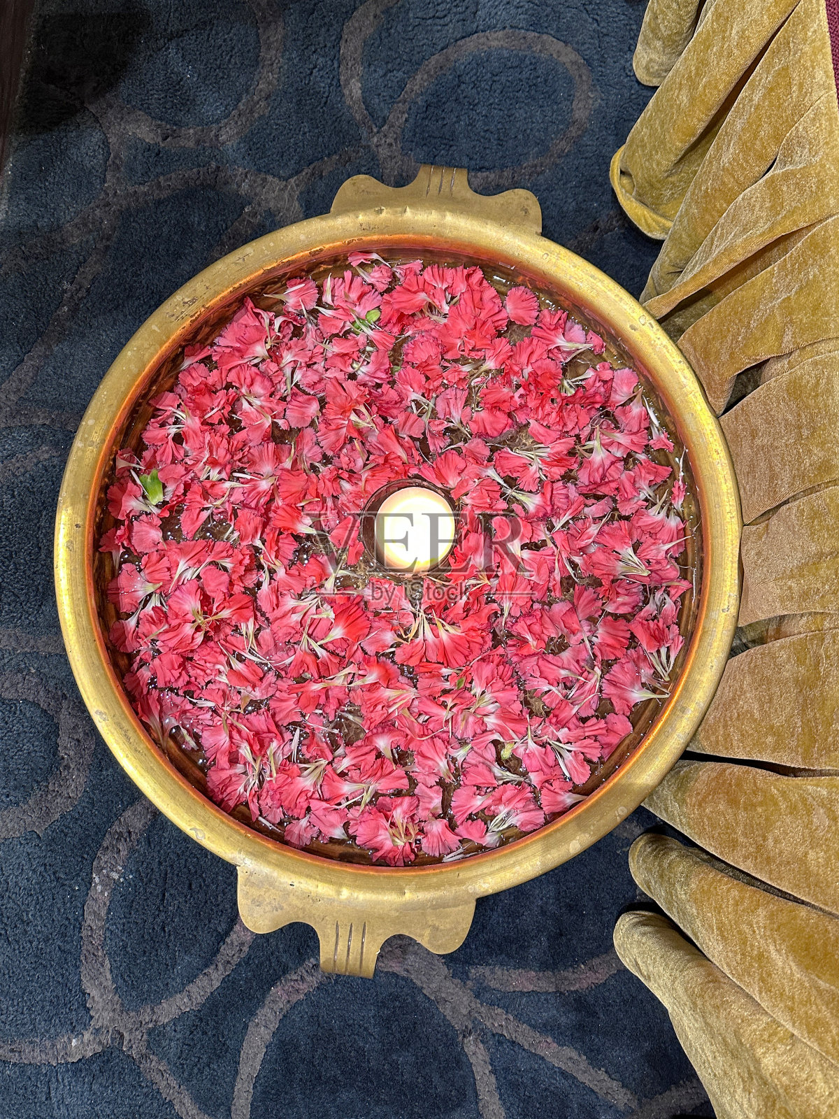 暗粉色康乃馨(石竹)花瓣环绕的蜡烛被照亮的形象漂浮在水中，uruli / urli(金属水盘)，传统的印度家庭，酒店或寺庙欢迎客人，高架视图照片摄影图片