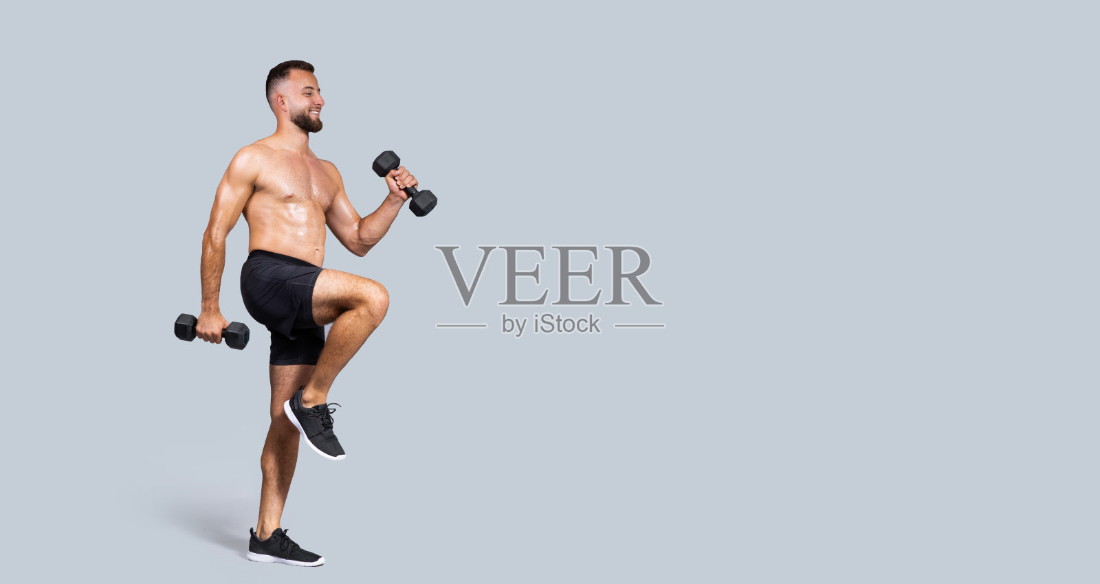 高兴的汗水强壮的肌肉千禧一代的欧洲人有胡子，裸露的躯干做哑铃练习照片摄影图片