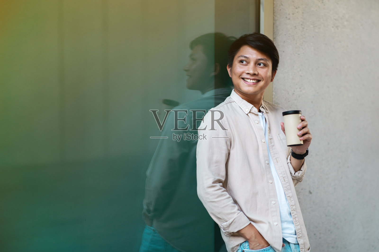 乐观的亚洲年轻人喝着咖啡，在商场摆姿势照片摄影图片