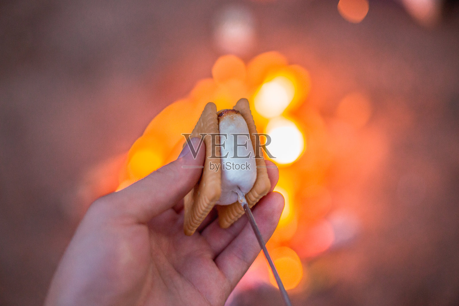 近距离的手拿着棉花糖和饼干做的S'more，在背景火照片摄影图片