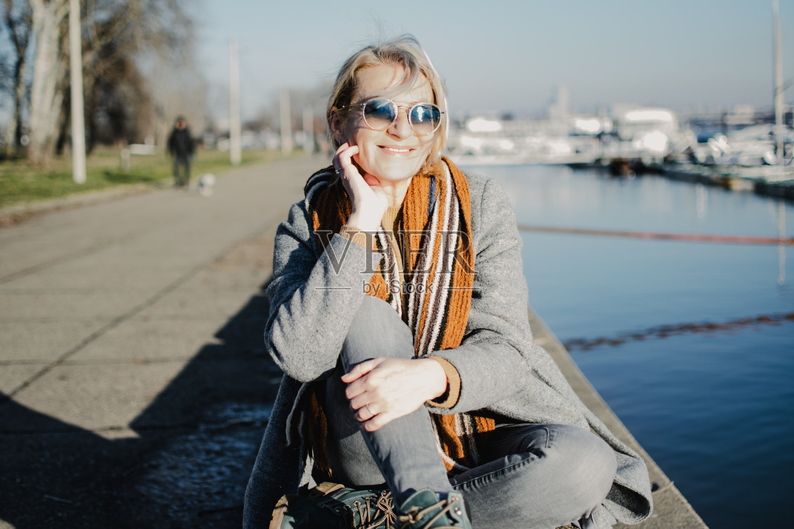 一位戴着墨镜的成熟金发女子坐在河岸上照片摄影图片