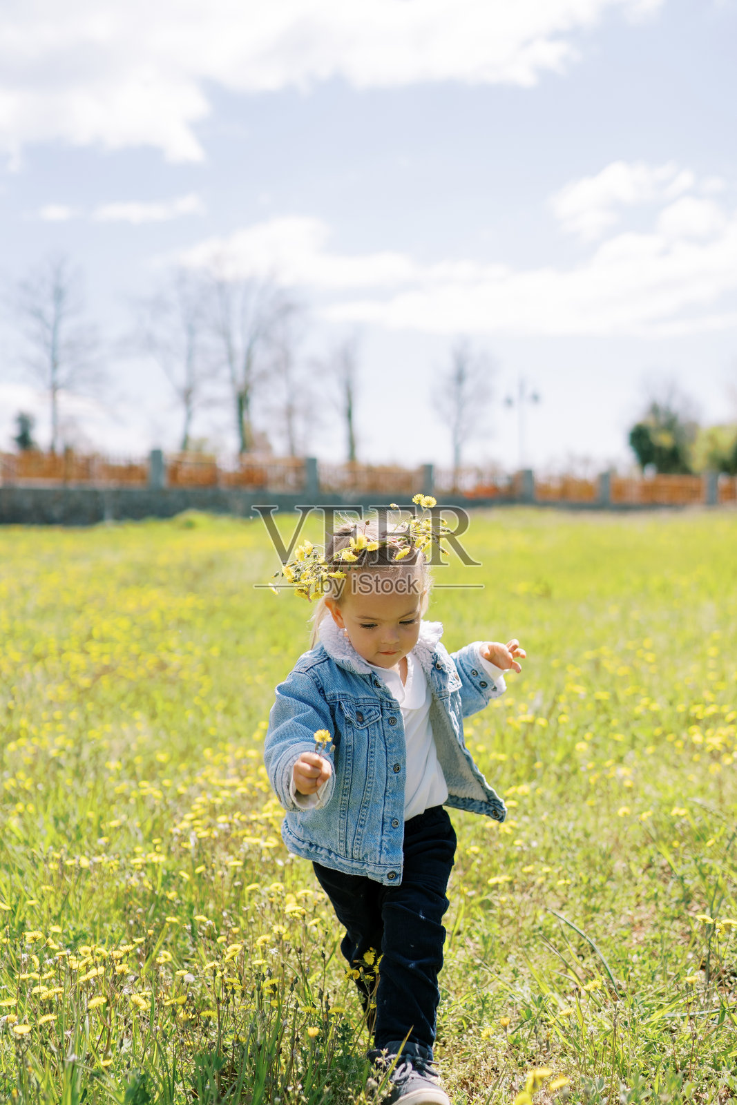 戴着花环的小女孩走在鲜花盛开的草坪上，低头看着自己的脚照片摄影图片