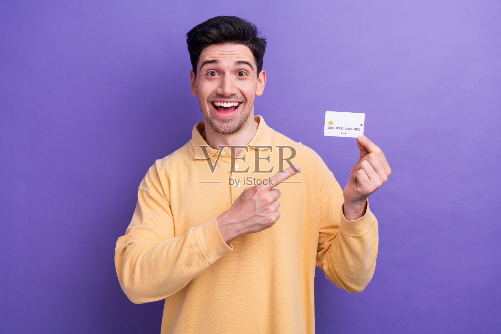 印象深刻的时髦的家伙穿黄色马球显示手指信用卡孤立的紫色背景的照片照片摄影图片
