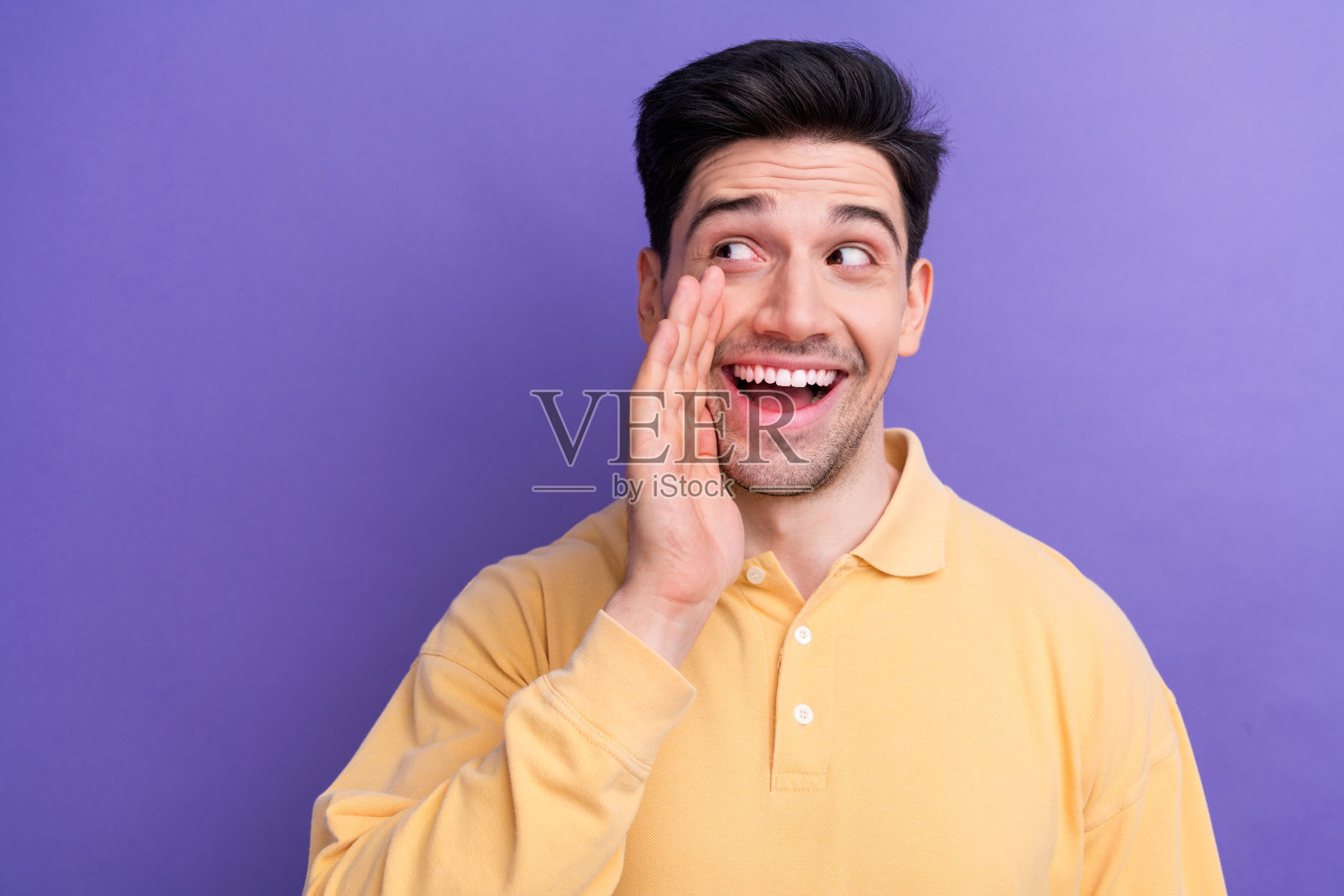 照片中心情好兴奋的小伙子穿着黄色polo衫手臂口吐秘密，看着空旷孤立的紫罗兰色背景照片摄影图片