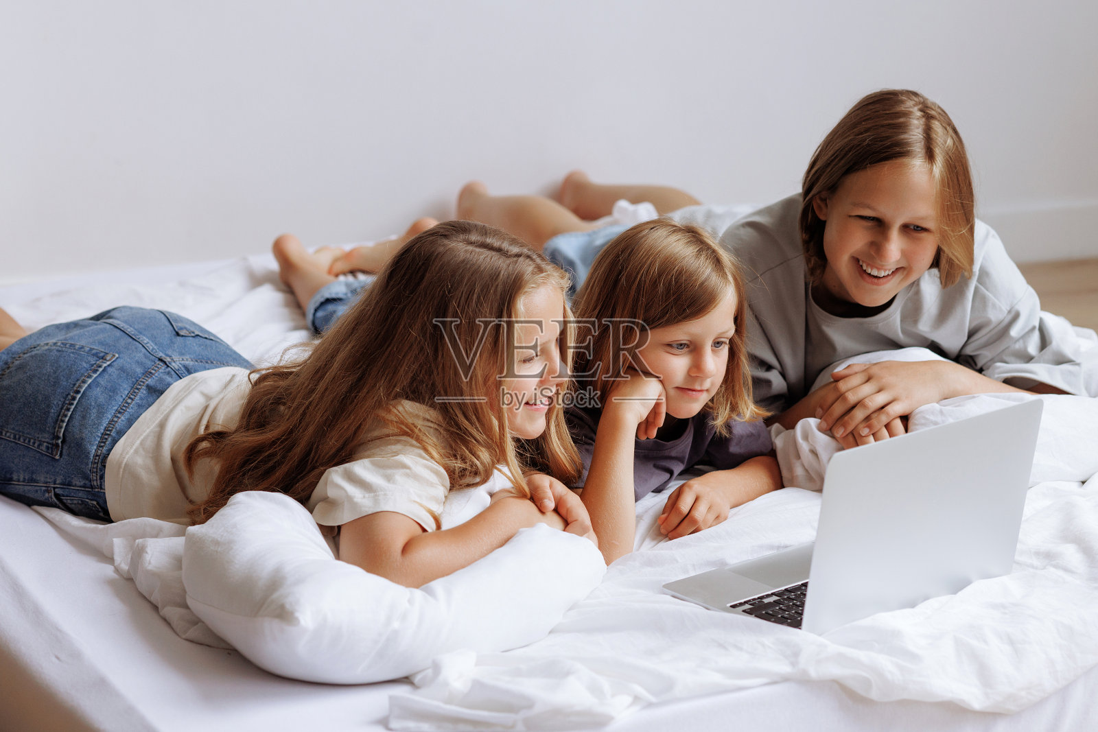 三个十几岁的女孩拿着笔记本电脑躺在床上。照片摄影图片