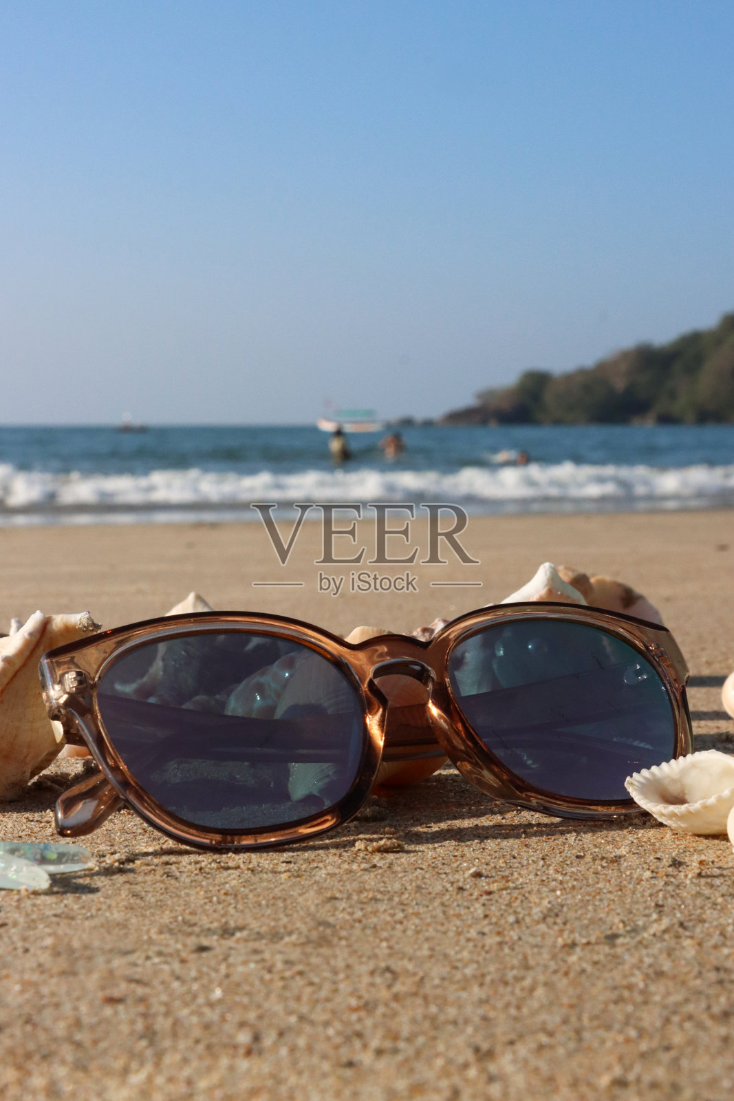 彩色玳瑁镜框，金色沙滩上的彩色太阳镜，周围是贝壳和海星，阳光明媚的沙滩，退潮时的波浪，大海和海岸线，重点放在前景，复制空间照片摄影图片