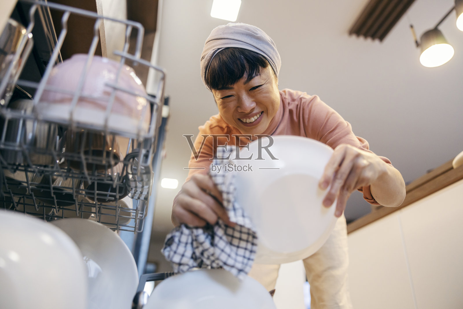 一位快乐的亚洲中年家庭主妇正在洗碗和卸洗碗机。照片摄影图片