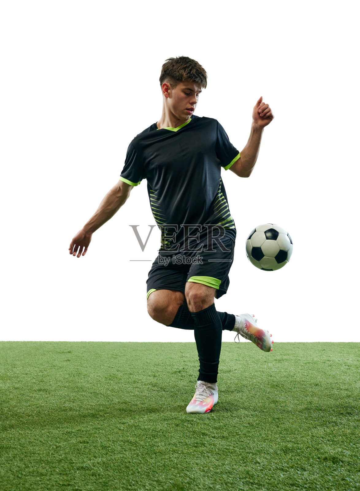 年轻好强的男子，带着球踢着足球，在白色背景的草地地板上单独训练照片摄影图片