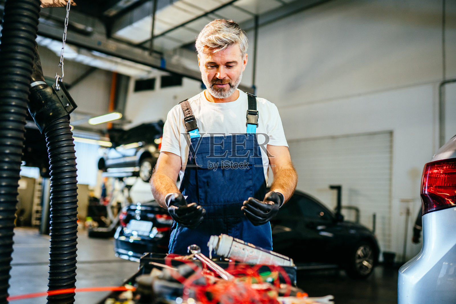 帅气的男工人找到了完美的工具。汽车修理工拿起修理汽车的工具。现代车间。汽车服务、维修、保养与人的理念。照片摄影图片