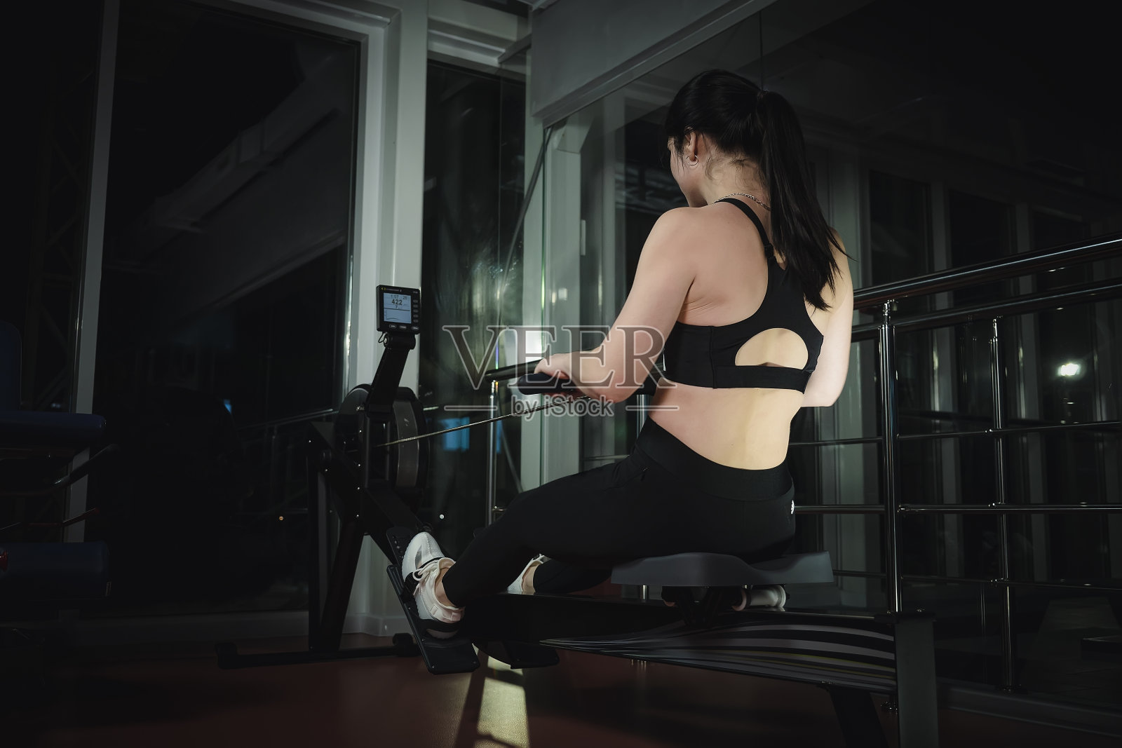 穿着运动服的黑发女子坐在模拟划船运动机上。功能训练照片摄影图片