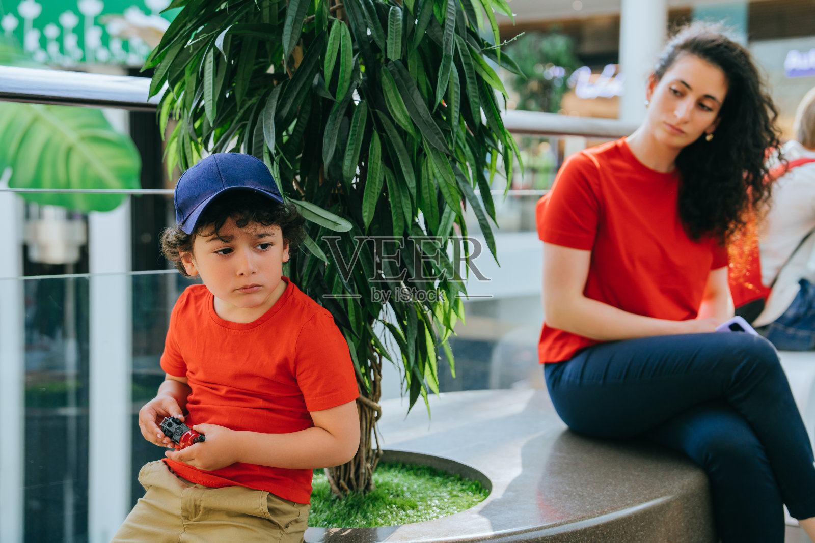 一个戴着帽子的小男孩坐在商场里的一个女人身边，家庭时光和现代生活方式照片摄影图片