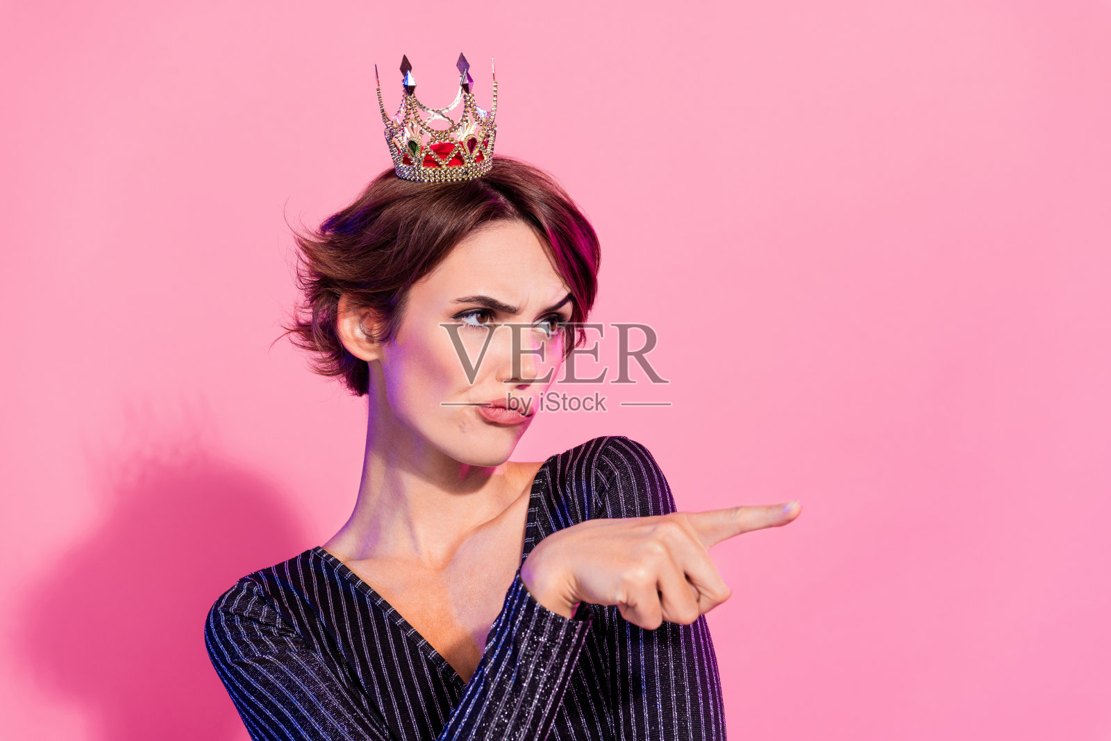 照片中可疑的不信任的女士戴着迷人的服装皇冠，看起来手指空白，孤立的粉红色背景照片摄影图片