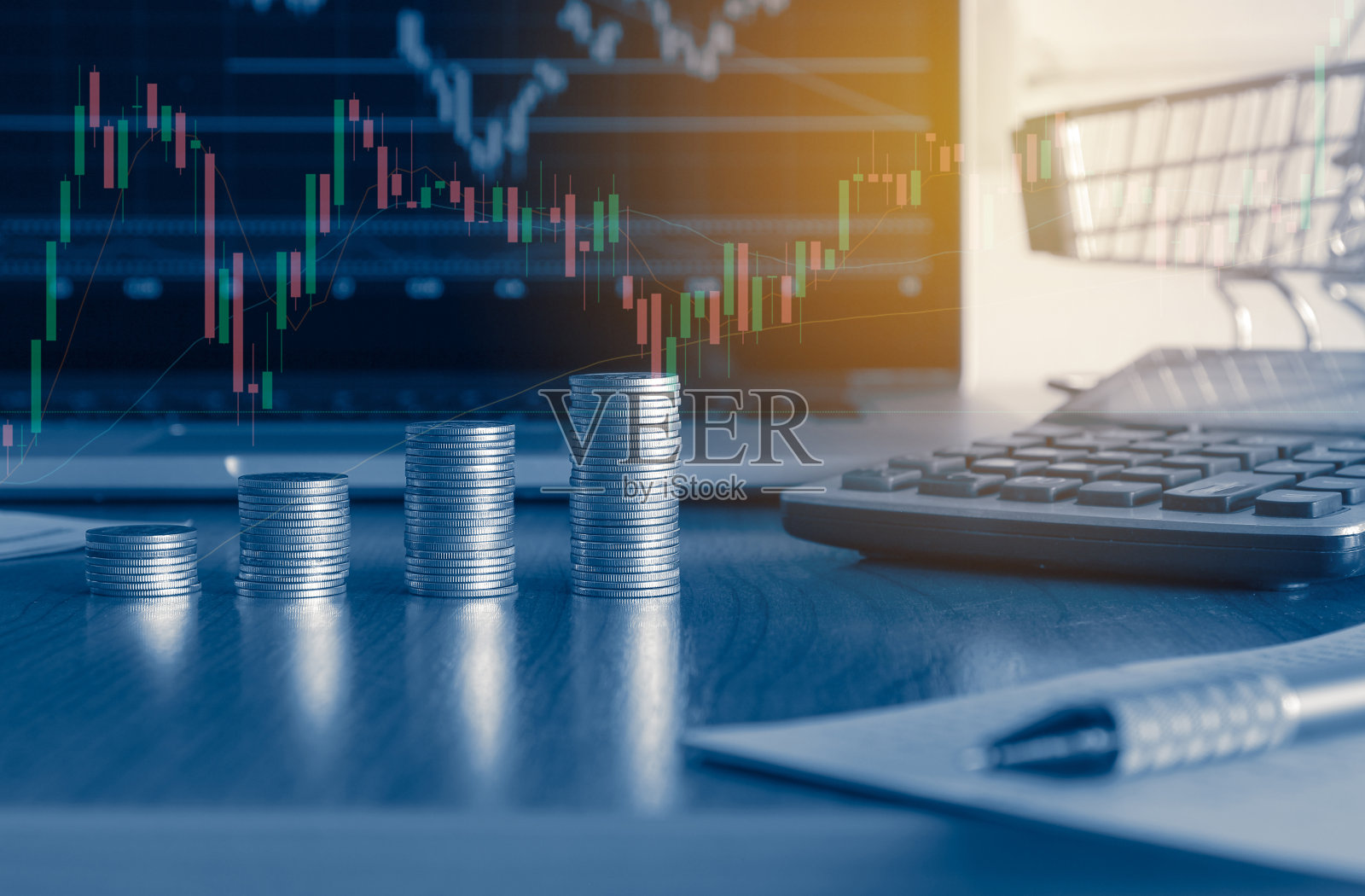 叠钱硬币与小购物车和笔记本电脑在后台打开交易图表，商业和金融的概念。照片摄影图片