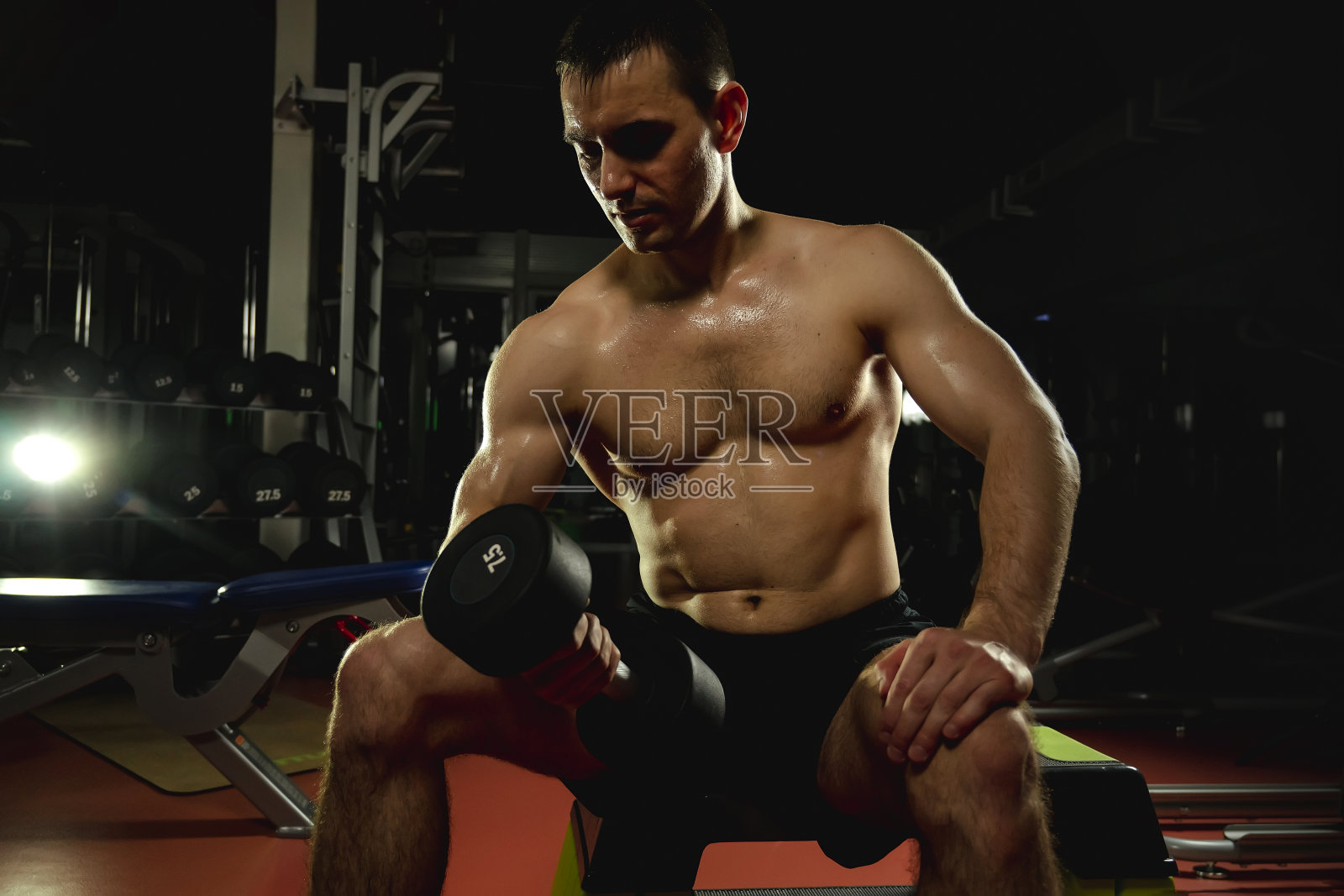 健美运动员用哑铃做肱二头肌的负重锻炼。运动和训练的概念。肌肉男在黑暗的健身房拿着哑铃，运动生活方式的概念。照片摄影图片