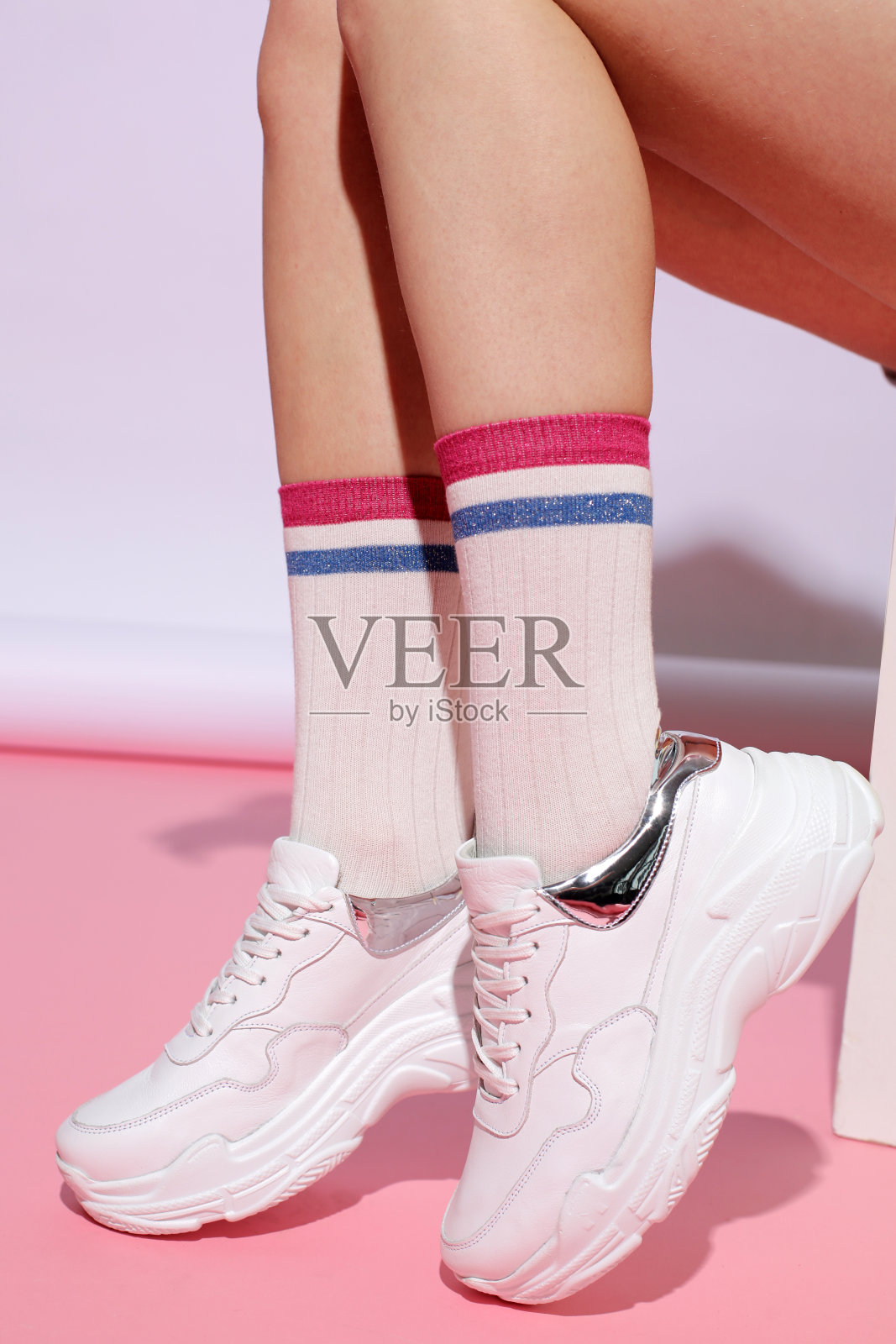 女性的腿穿着时尚的运动鞋和袜子，颜色背景与硬阴影。广告的鞋子照片摄影图片