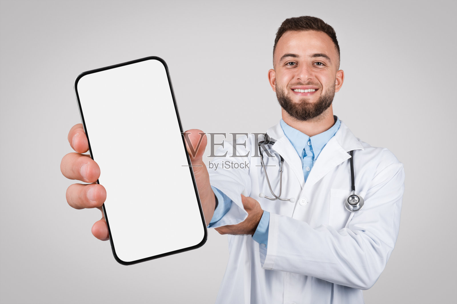 男医生拿着大手机，灰色背景上的空白屏幕照片摄影图片