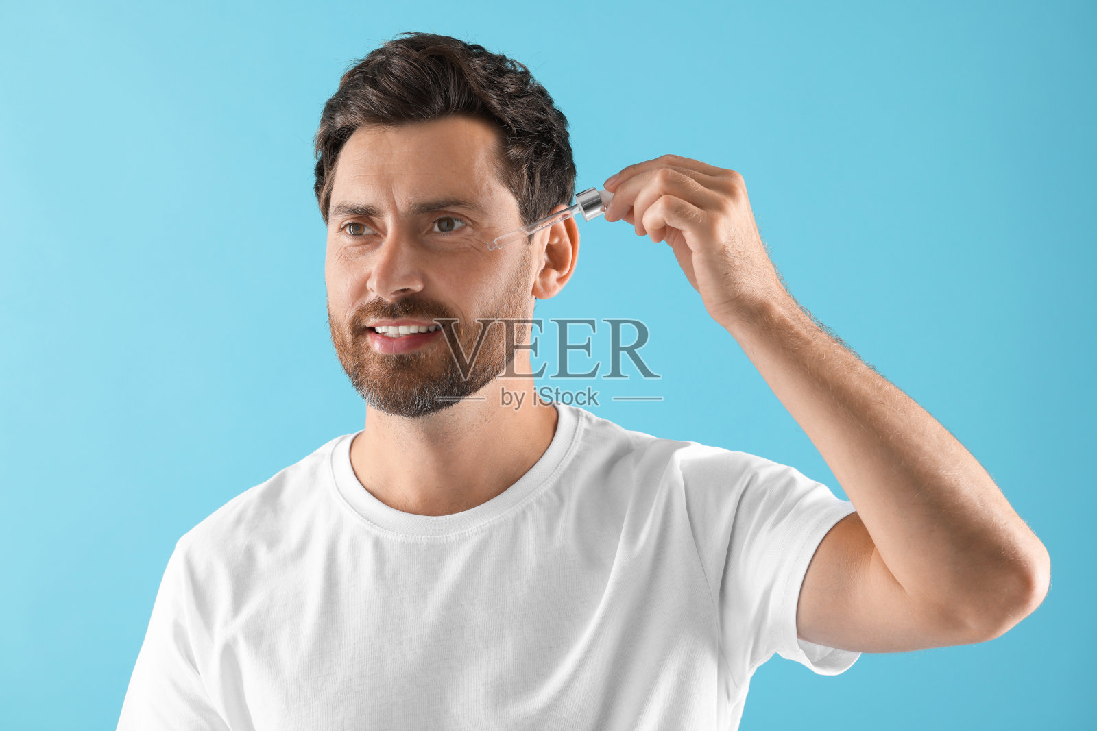 微笑的男子在浅蓝色的背景上给脸上涂化妆品精华液照片摄影图片