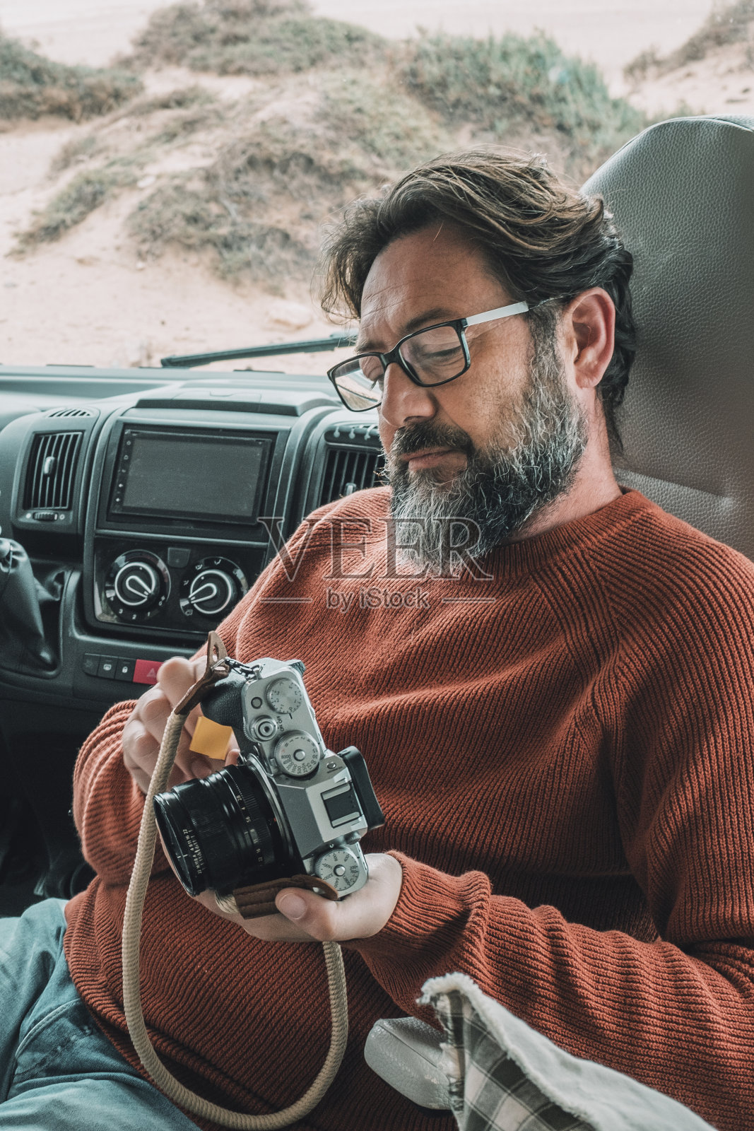 一名男子坐在露营车上观察用相机拍摄的照片。男旅客在他的带轮子的房子里放松照片摄影图片