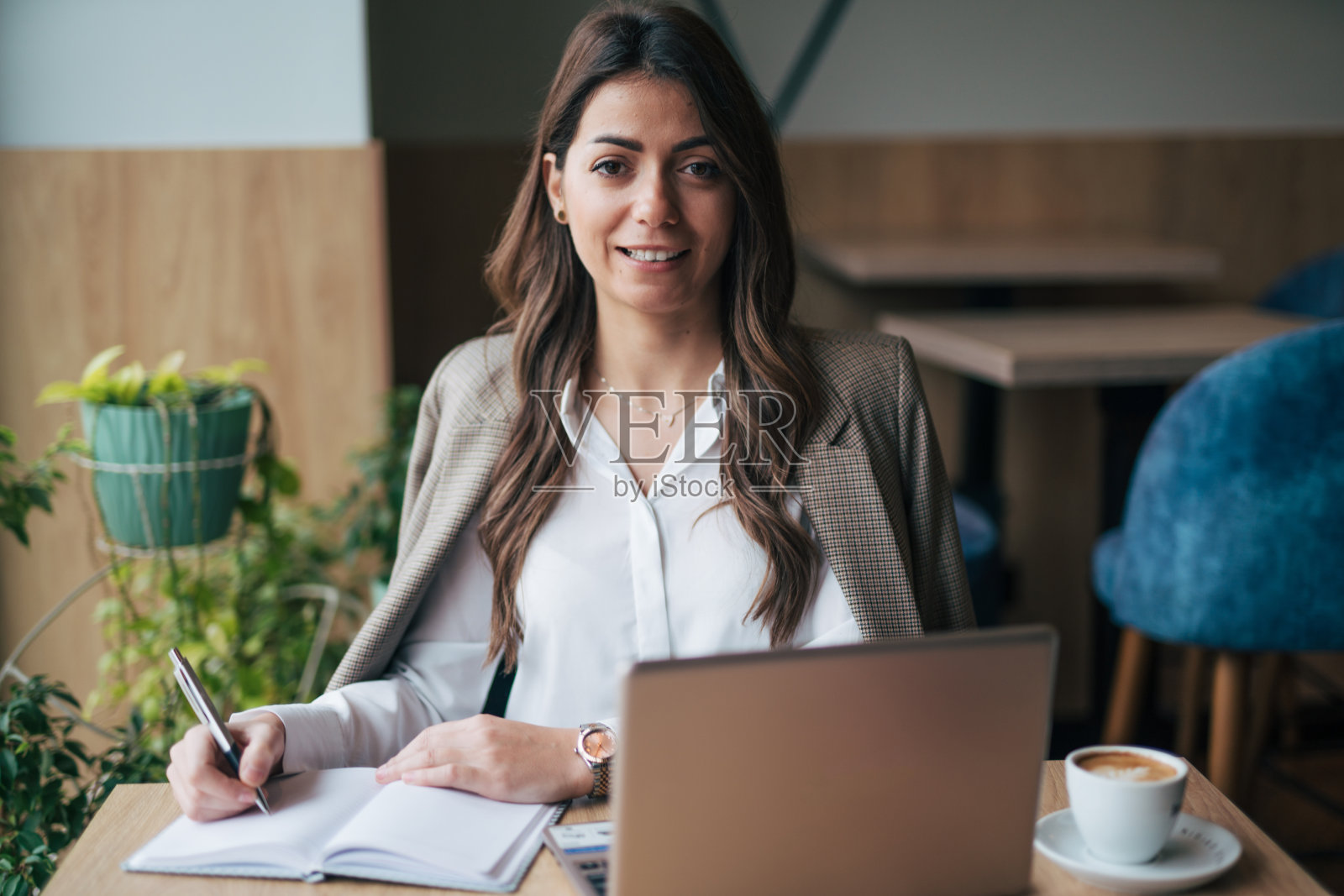 一个漂亮的女商人拿着笔记本电脑和一杯咖啡坐在咖啡馆里照片摄影图片