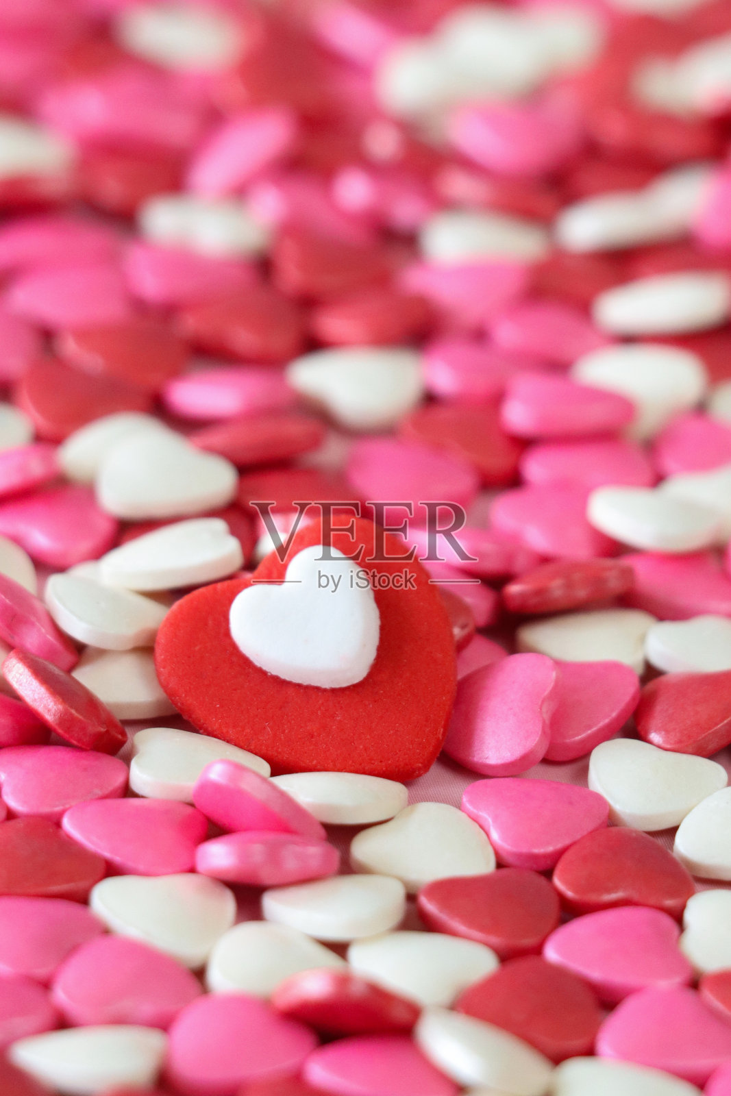全帧图像的红色糖霜心堆上的红色，粉红色和白色的糖果心，情人节装饰，斑驳的粉红色背景，高架视图，重点在前景，情人节和浪漫的概念照片摄影图片