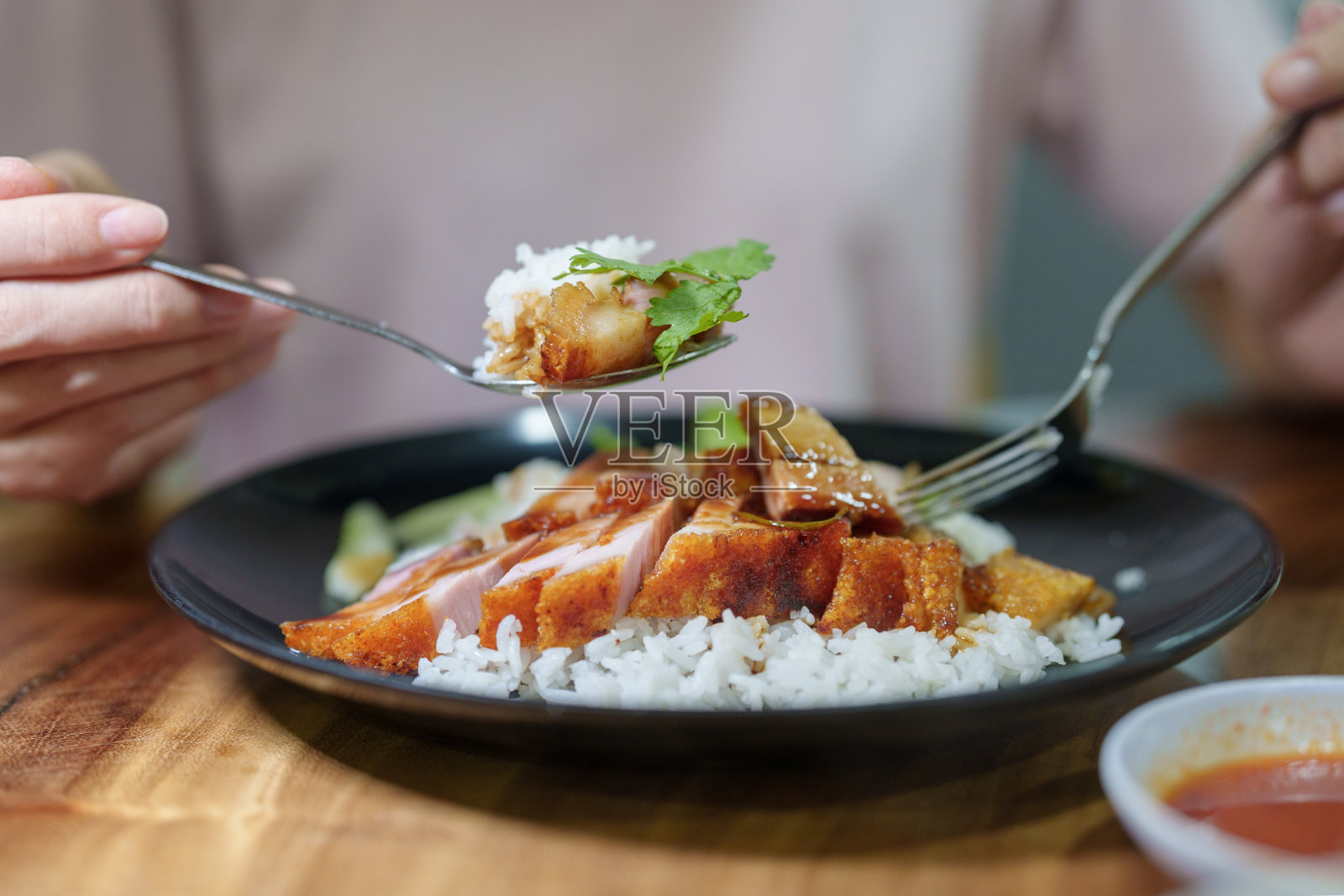 在特写镜头中，一位年轻的亚洲妇女正在享用一盘亚洲风味的脆皮五花肉饭。照片摄影图片