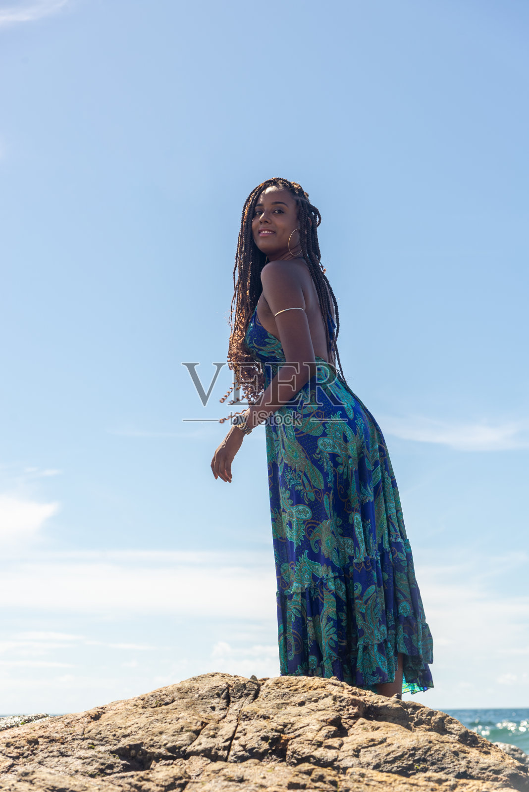 一个美丽的女人，扎着辫子，穿着蓝色的衣服，站在海滩的岩石上摆姿势拍照照片摄影图片
