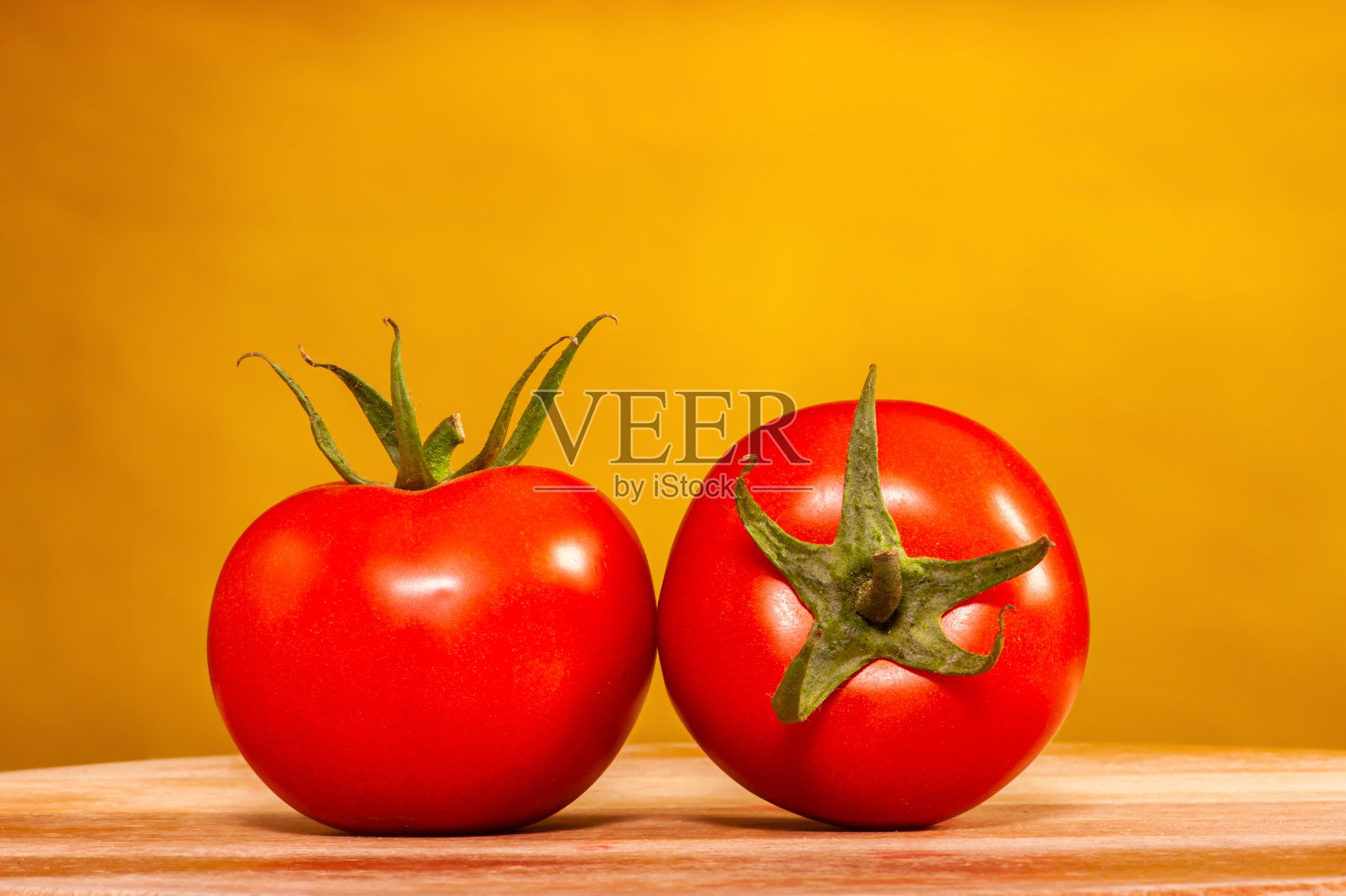 两个西红柿放在砧板上，背景是彩色的黄色照片摄影图片