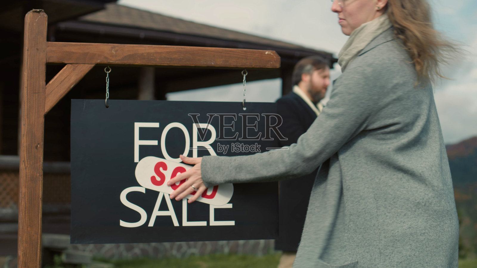 女房地产经纪人把出售标签贴在待售标牌上照片摄影图片