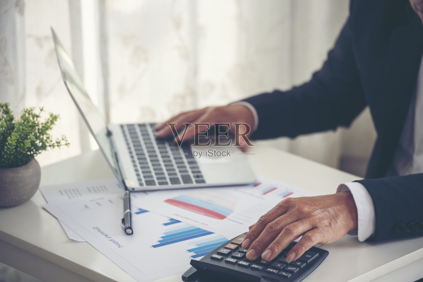 特写商人双手工作使用笔记本电脑财务业务文件阅读报告文书工作电子表格在办公桌上。男人用手打键盘，在办公笔记上写，查财务图表照片摄影图片