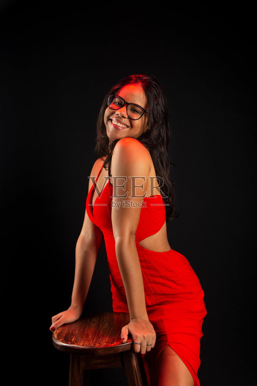 漂亮的年轻女子戴着处方眼镜，穿着红衣服，摆姿势拍照。照片摄影图片