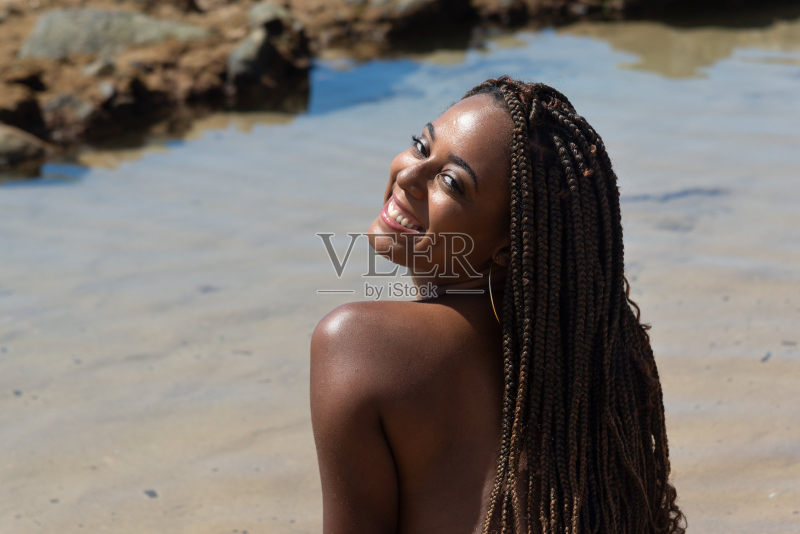 一个美丽女人的半封闭肖像，扎着辫子，背对着镜头。在海滩上晒日光浴。照片摄影图片